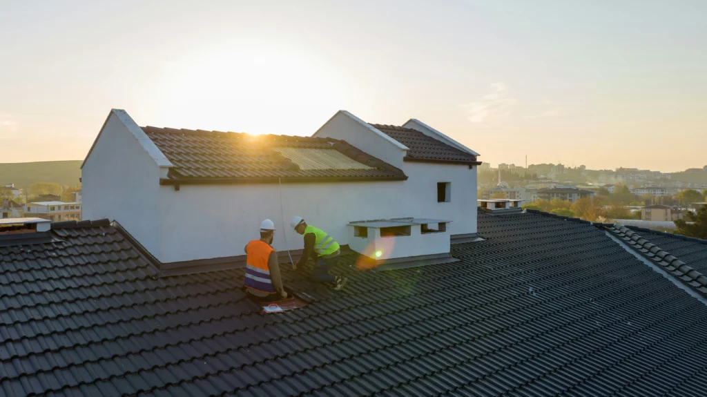 A white house with two men standing on the roof cleaning it.