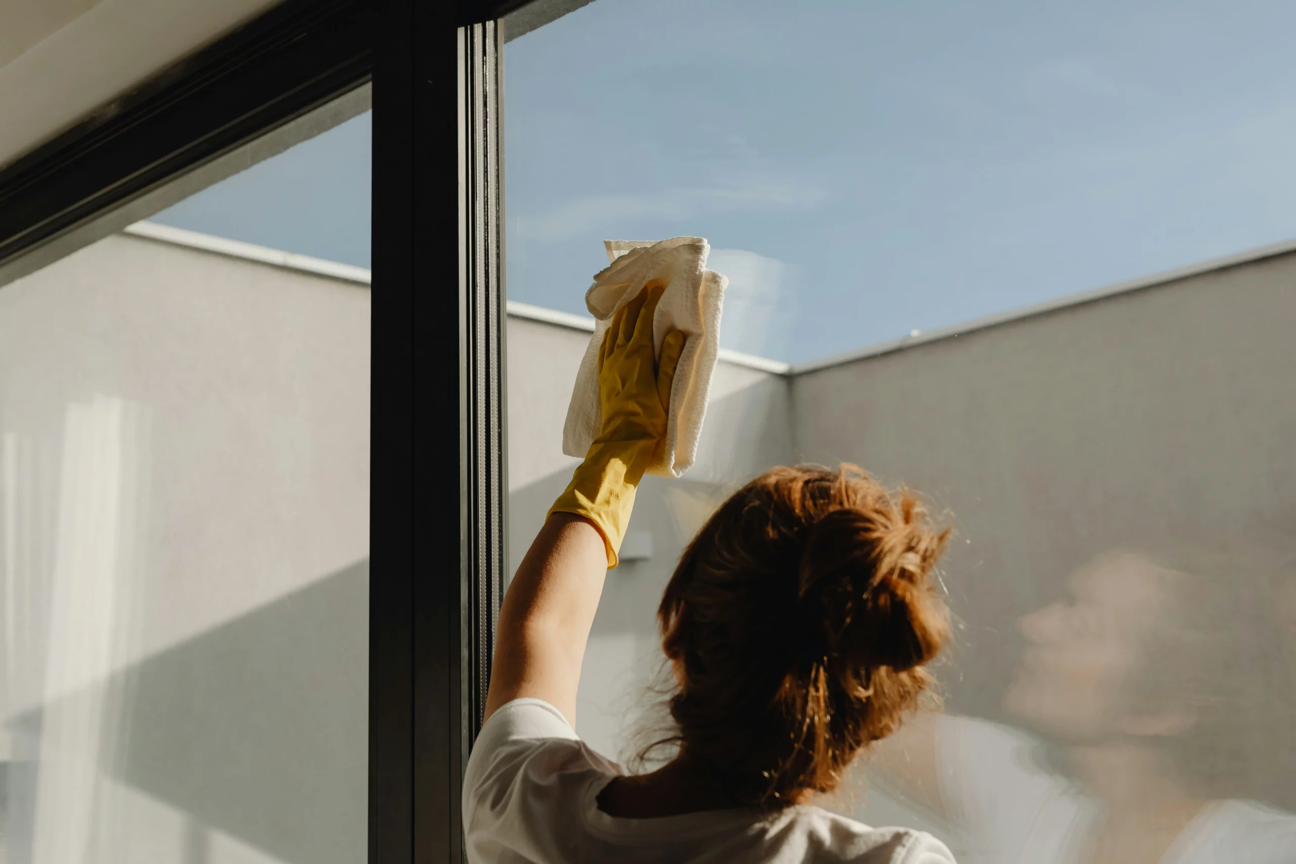 A woman with gloves and a towel providing Window Cleaning Pearland services.