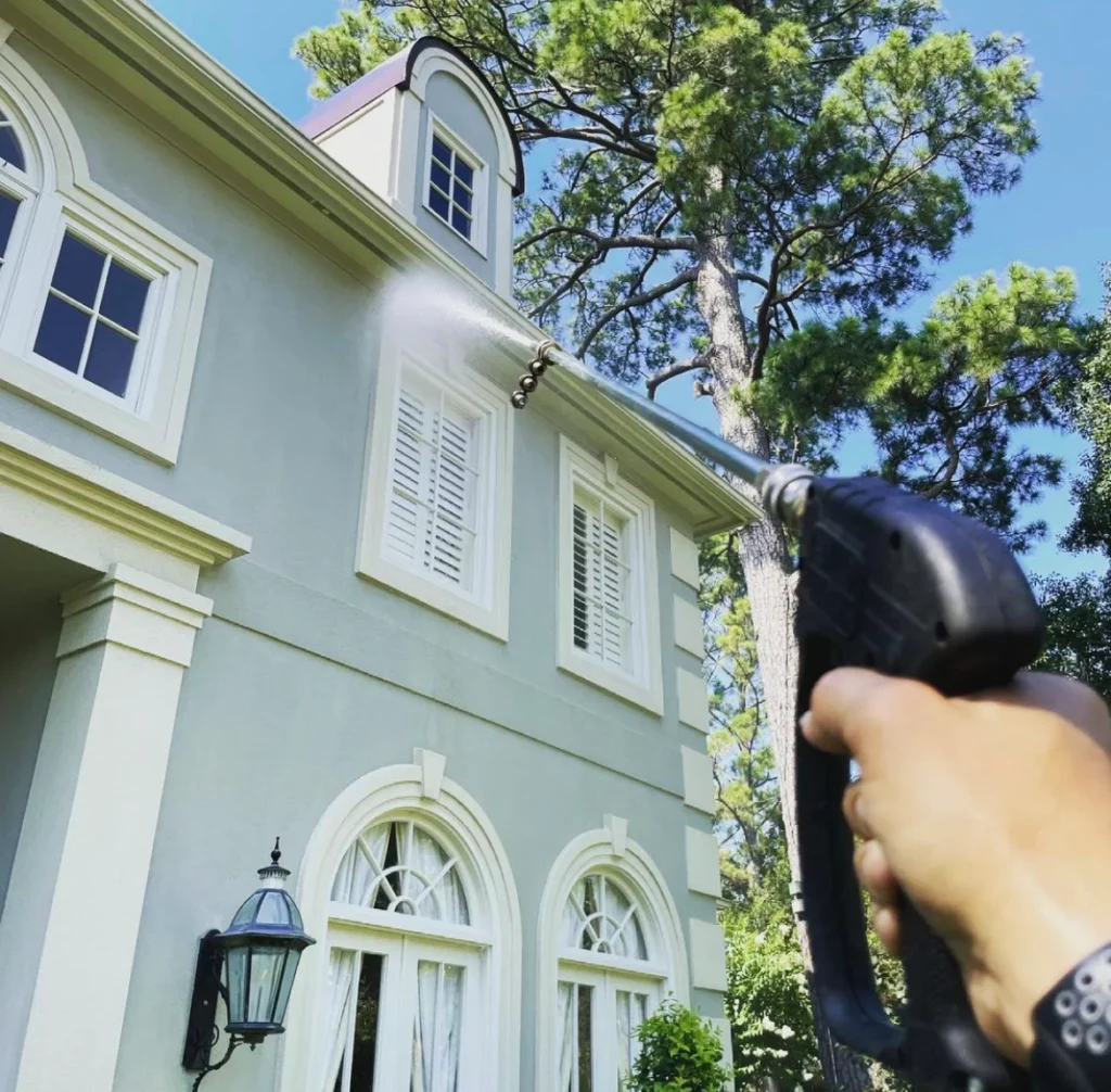 A hand using a pressure washer to wash a second story of a house demonstrating how often you should pressure wash your house.