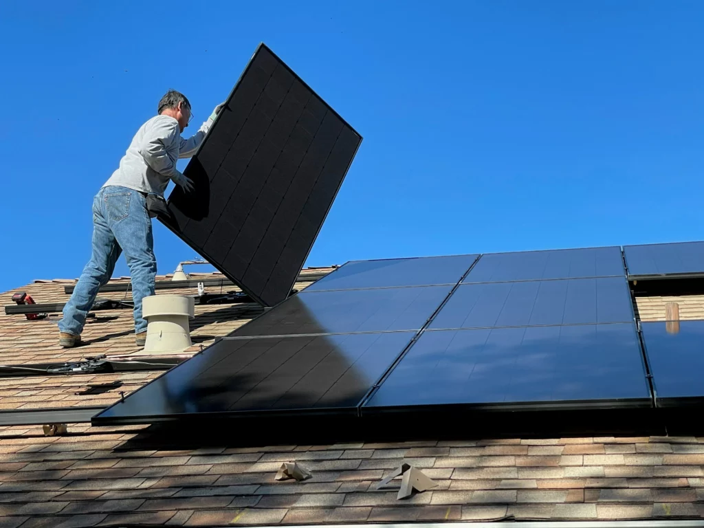 A man installing a solar panel on a roof with other power wash solar panels.