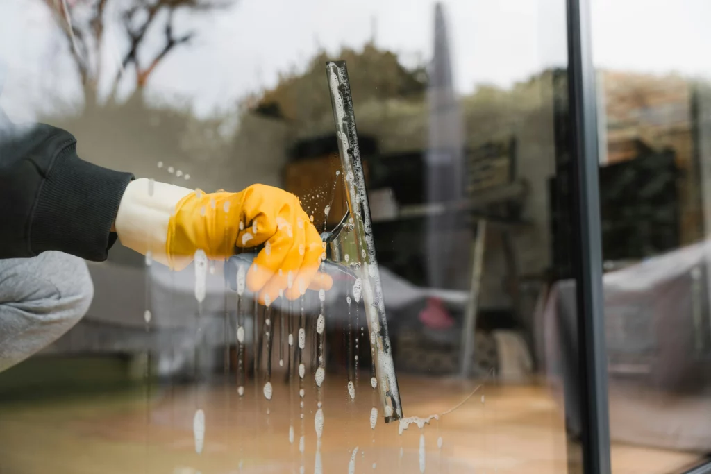 A hand with a yellow glove cleaning a window with a squeegee.