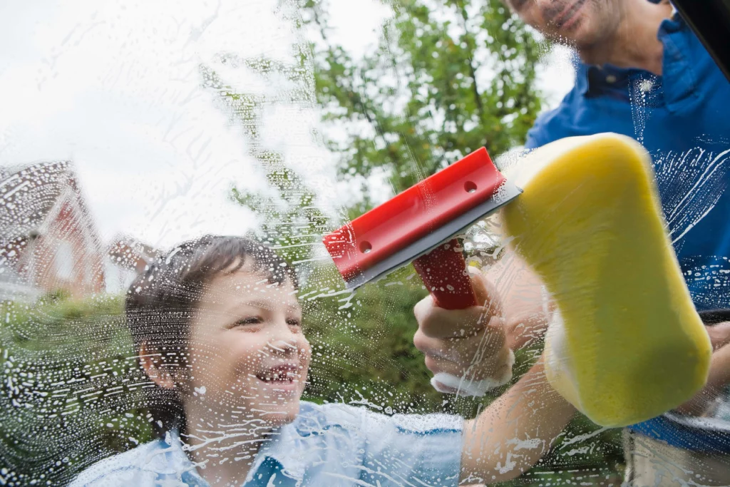 A man helping a child Window Cleaning with a Squeegee.