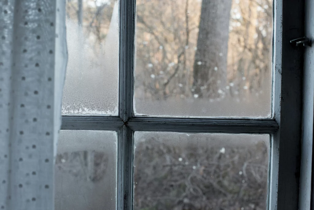 A old white window with condensation building up on the glass indicating that the Window Seals might need to be replaced.