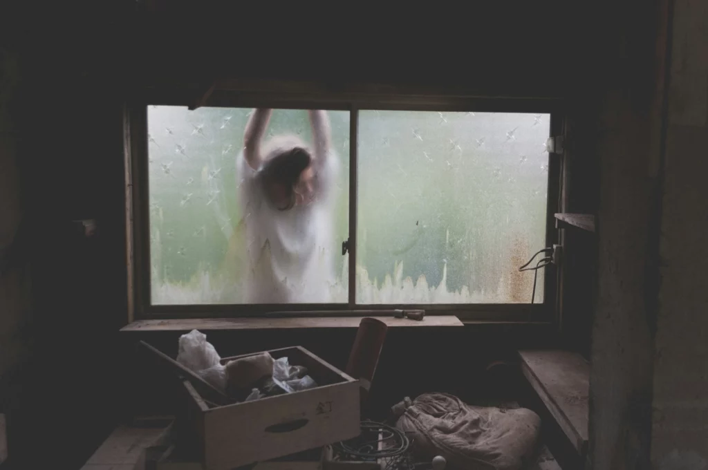 A woman standing beside a dirty basement window.