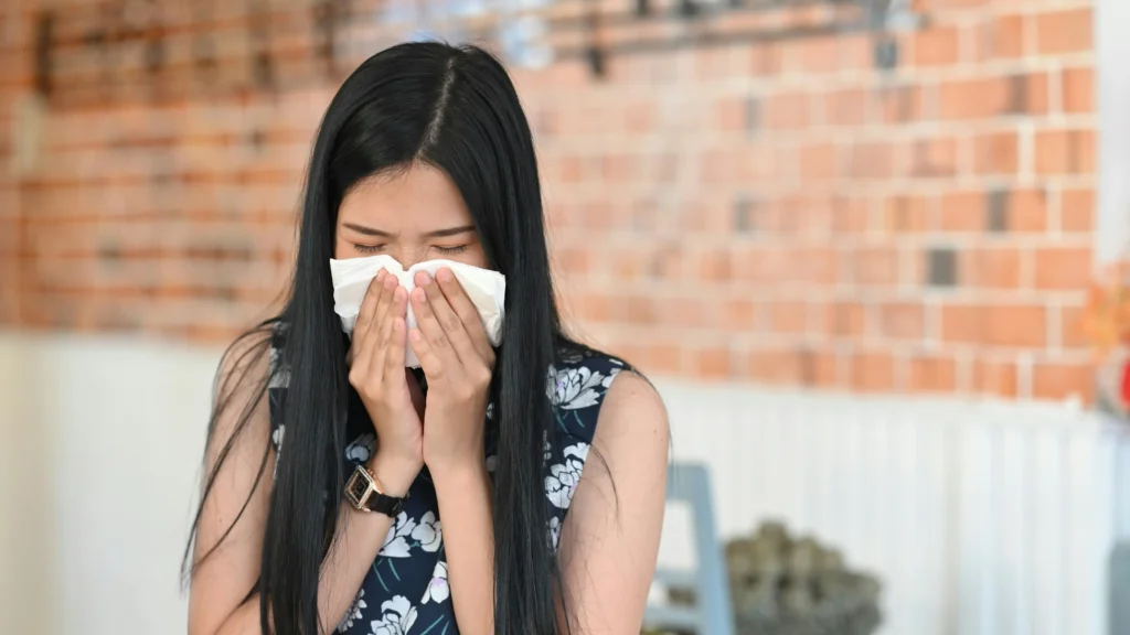 A woman sneezing into a tissue demonstrating why it is important to know the best time to open windows during allergy season.