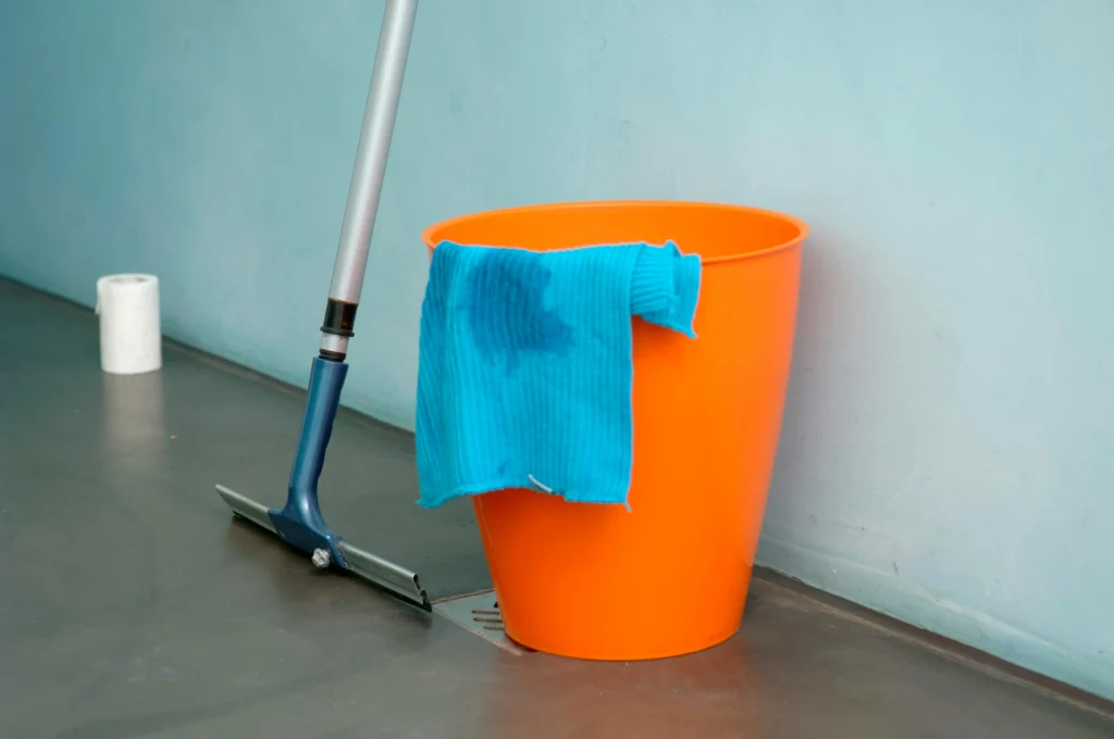 A picture of an orange bucket and a blue towel and squeegee to clean window screens.