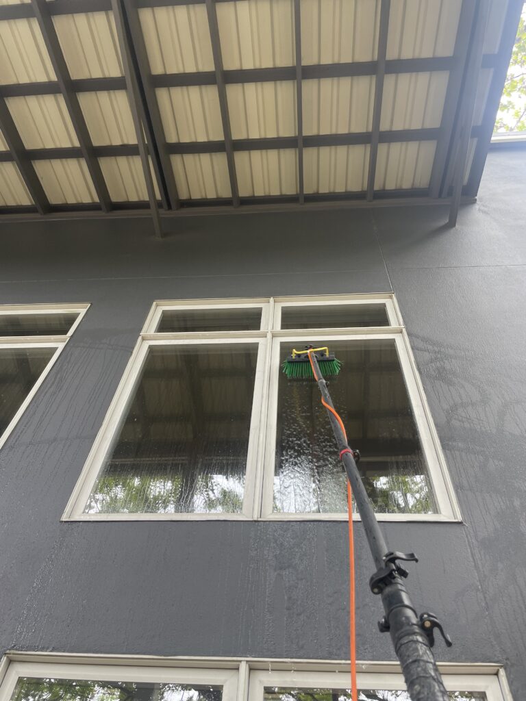 Window Cleaning Tools - Long Black Window Cleaning Pole with Brush Attachment Being Used to Clean Second Floor Window of House