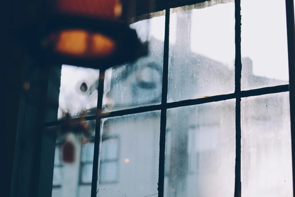 Foggy window with smudges and dusty glass reflecting a building outside in dim interior lighting