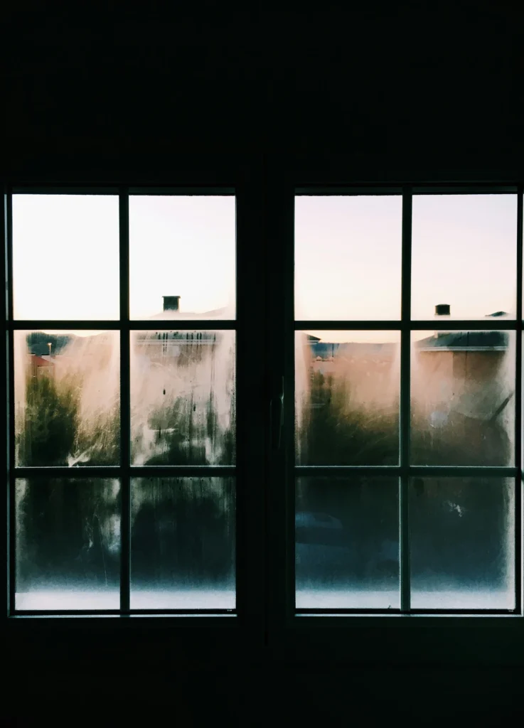 Why are my windows foggy view of a window with condensation and smudges overlooking houses at sunset